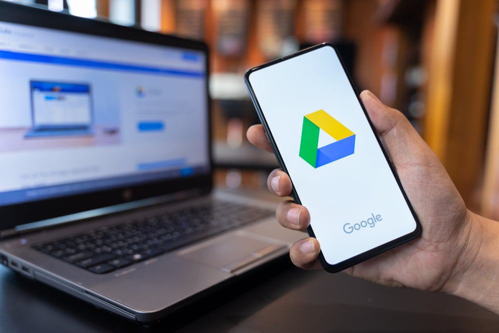 Celular com o logotipo do serviço de armazenamento na nuvem Google Drive com um computador ao fundo