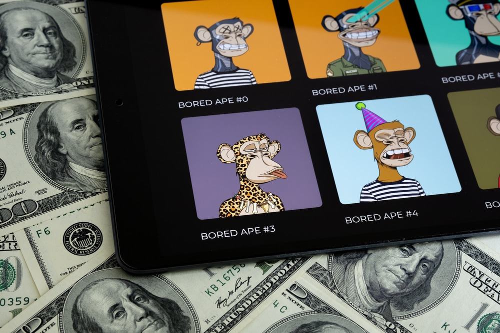 Coleção de NFTs Bored Ape vista na tela de um tablet com notas de 100 dólares ao fundo