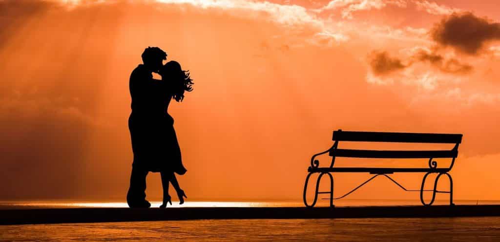 Silhueta de um casal se beijando próximo a um banco ao pôr do Sol