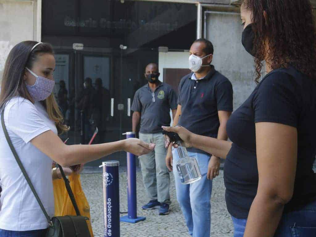 Estudante com máscara facial aplica álcool em gel nas mãos na entrada do Enem