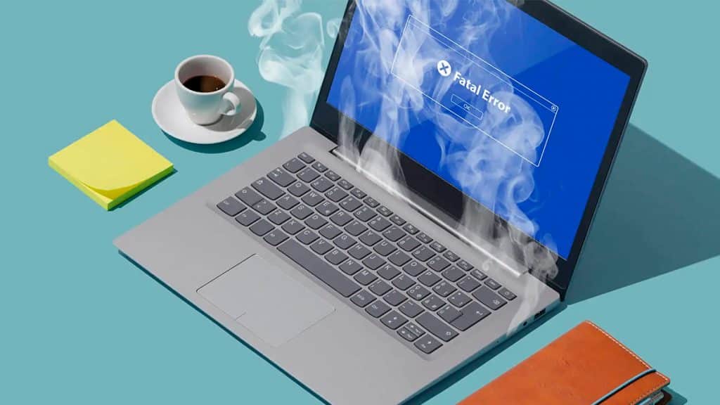 Notebook superaquecendo ao lado de café, bloco de post-its e caderno de anotações