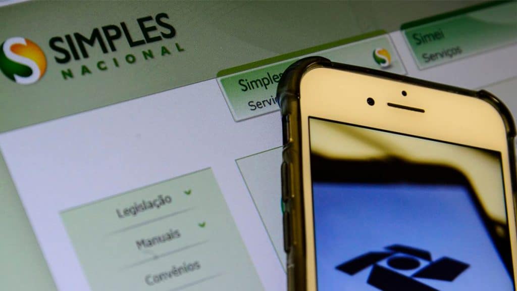 Celular com imagem da Receita Federal em frente a computador com página do Simples Nacional aberta