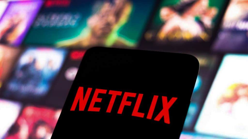 Celular com logomarca Netflix e pôsteres de produções do serviço de streaming ao fundo