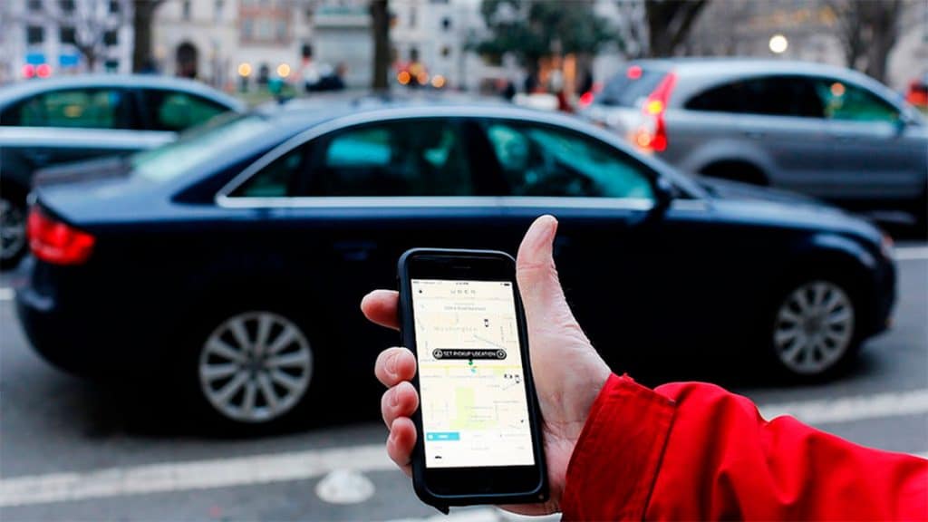 Pessoa com celular na mão esperando, na beira de uma calçada, Uber chegar