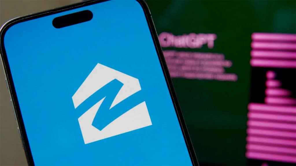 Celular com logomarca da Zillow na tela e, ao fundo, computador com ChatGPT aberto