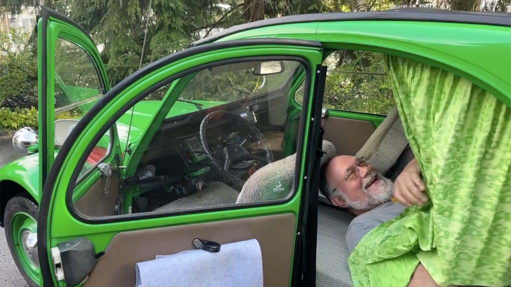 Homem deitado no banco traseiro de um Citroën 2CV que ele transformou em trailer