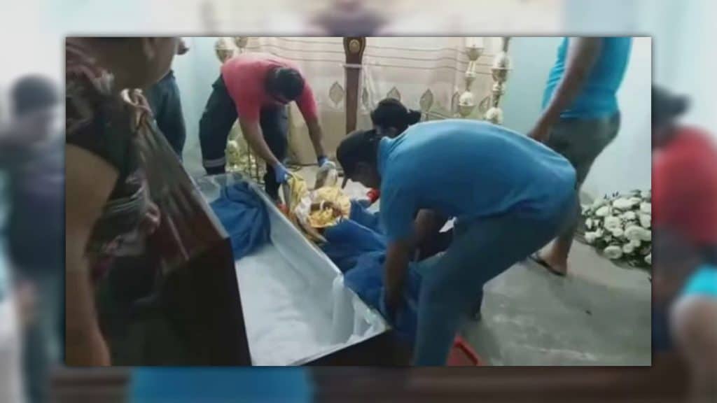 Familiares de idosa e paramédicos em volta do seu caixão durante velório