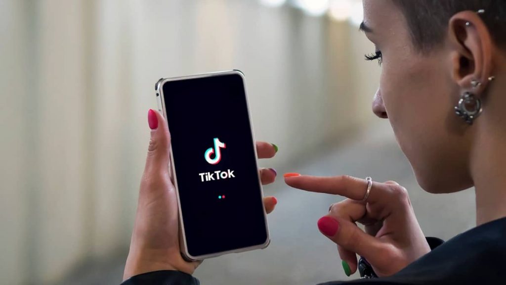 Mulher segurando celular com logomarca do TikTok e com dedo prestes a encostar na tela