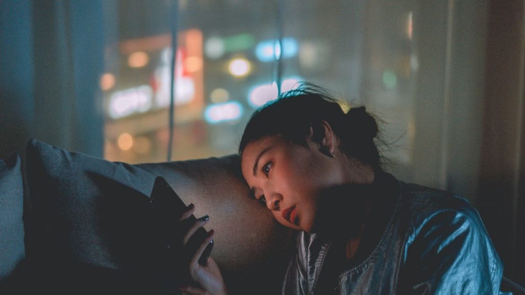 Mulher com celular no sofá e semblante triste