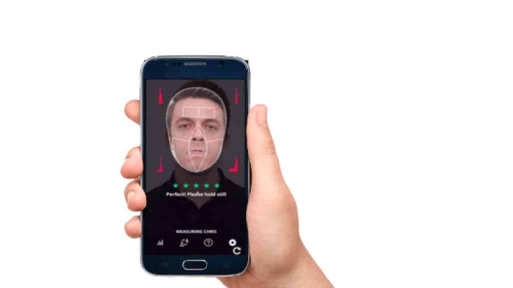 Imagem de uma mão segurando um celular com o reconhecimento facial de rosto de homem