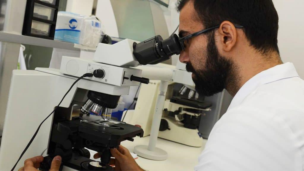 Homem olhando em microscópio num laboratório