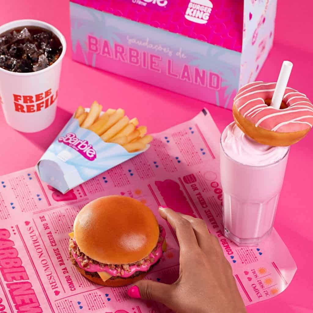 Imagem mostra lanche, copo de milkshake, batata frita e refrigerante e donut com itens rosa 
