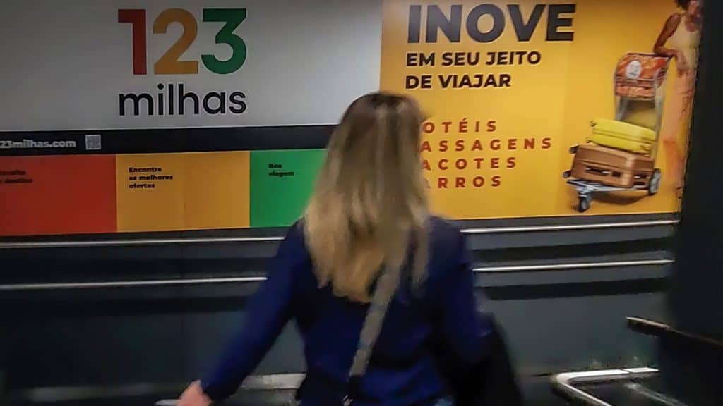 Mulher de costas passando por anúncio da 123 Milhas