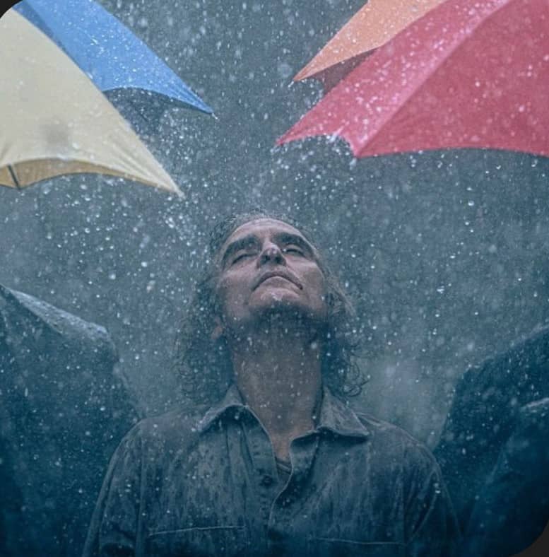 O ator Joaquin Phoenix caminha na chuva entre guarda-chuvas coloridos em cena do filme Coringa 2