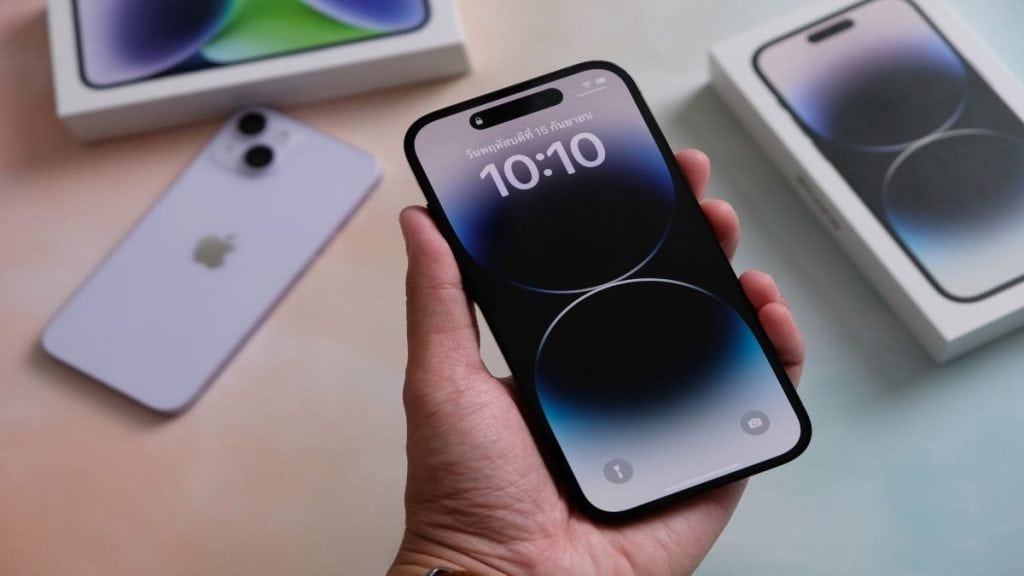 pessoa com iphone na mão e outros na mesa