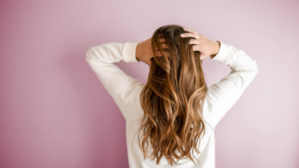 imagem mostra mulher de costas para a câmera e coçando o cabelo longo com a ponta dos dedos