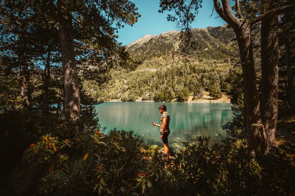 Homem em um lugar com montanhas e lago procurando sinal de celular
