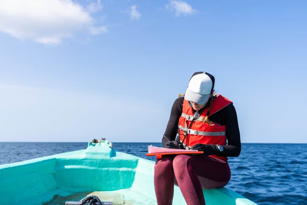 Bióloga Marinha sentada em um barco fazendo anotações