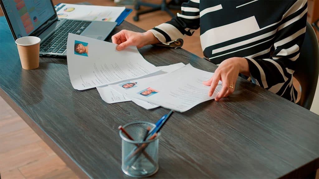 Candidatos usam truques para enganar IA de recrutamento A inteligência artificial está mudando a forma como candidatos buscam empregos e como selecionadores os escolhem. Segundo o Fórum Econômico Mundial, 90% dos empregadores já utilizam a IA para filtrar e classificar currículos. Pessoa mexendo em currículos num escritório