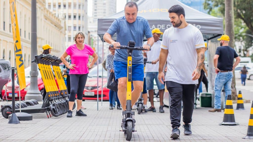 Funcionário da Whoosh ajudando homem a andar em patinete elétrica da empresa