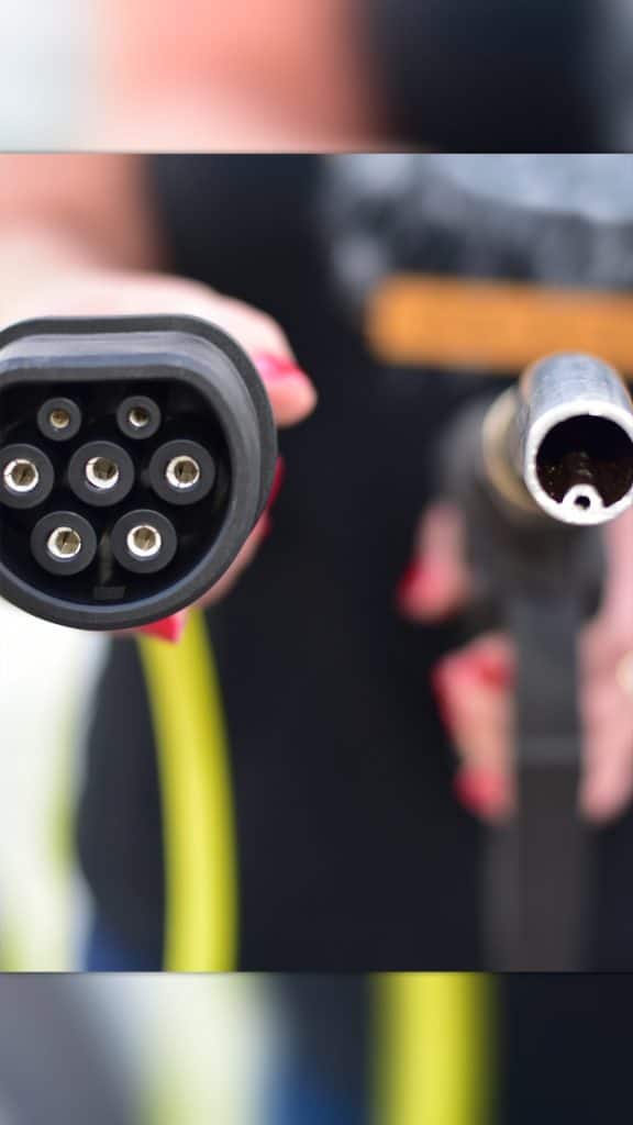 Pessoa segurando carregador de carro elétrico e mangueira de gasolina