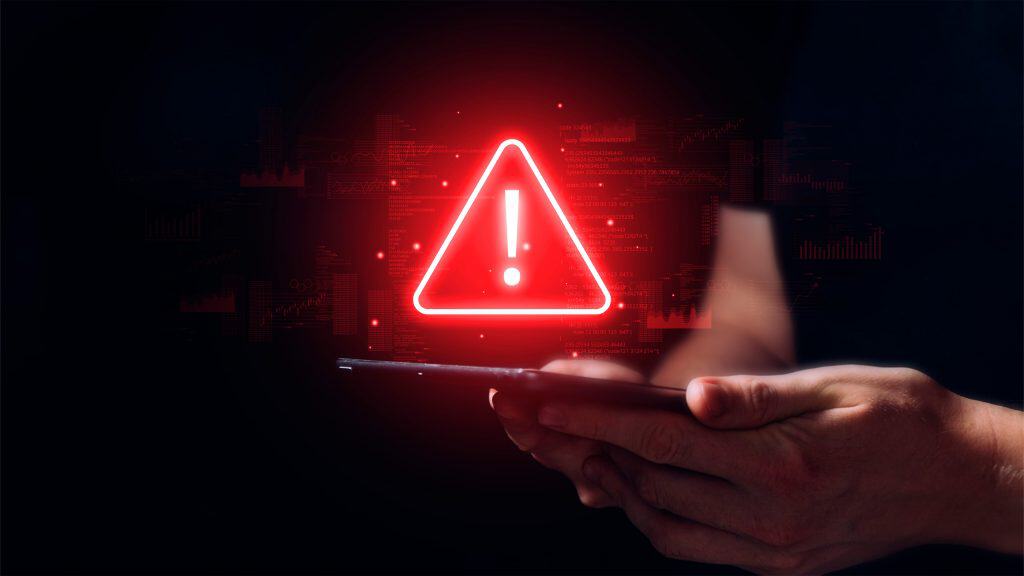 Pessoa usando celular com ilustração de sinal de alerta vermelho em cima do aparelho