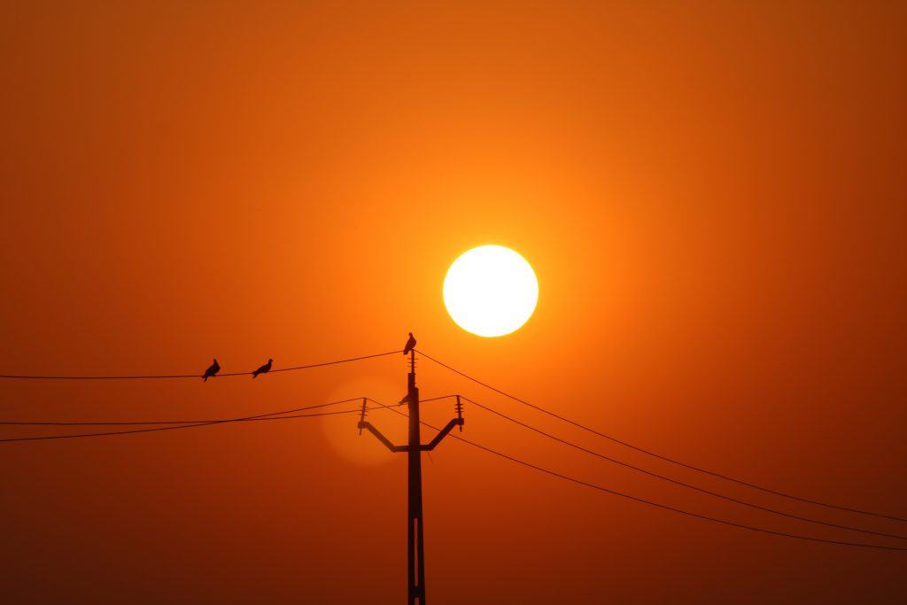 Sol ao fundo, com uma torre de energia elétrica mais próxima da câmera