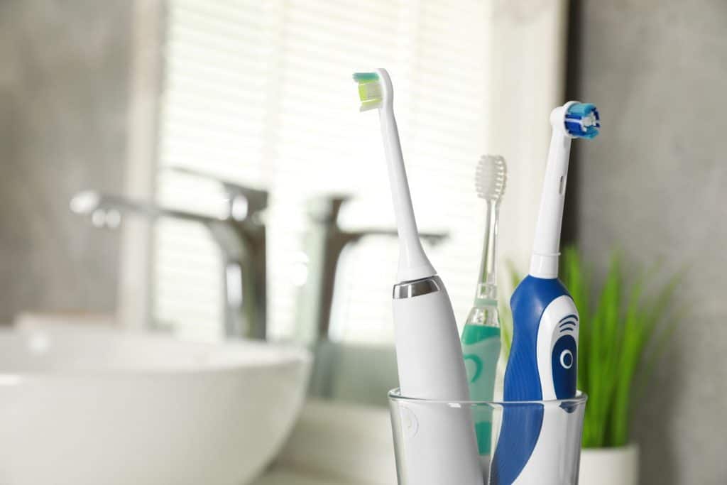 Escovas de dentes elétricas em um suporte de vidro dentro de casa, de perto. Espaço para texto.