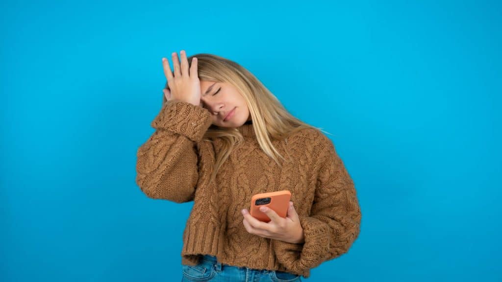 Menina adolescente infeliz cobrindo o rosto com as mãos e chorando enquanto está sentada no chão com o celular perto, uma criança adolescente frustrada e chateada sendo assediada ou intimidada online. 