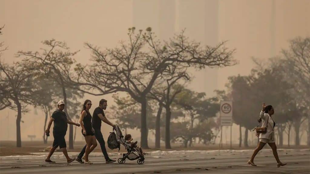 Pessoas andando na rua de uma cidade encoberta por fumaça de queimadas