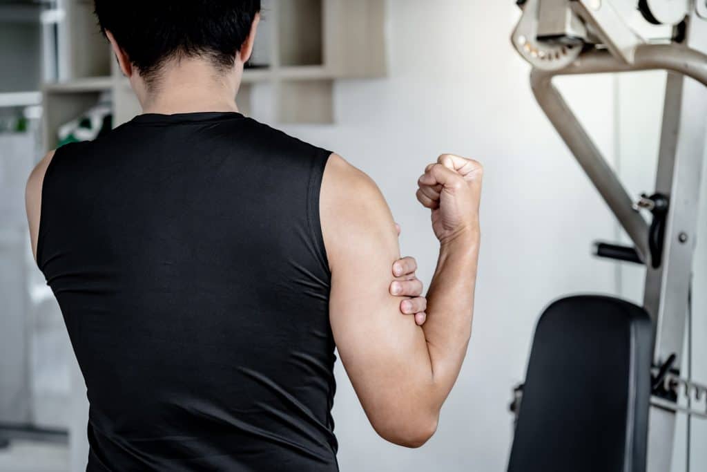 12 mudanças no corpo que você não deve ignorar, mesmo que pareçam pequenas O nosso corpo é um sistema complexo que envia sinais constantes ao cérebro sobre o estado de saúde. Uma dor de cabeça, um incômodo muscular ou uma alteração na pele podem parecer situações comuns, mas até essas pequenas mudanças físicas podem indicar o início de doenças graves ou crônicas. Imagem mostra um homem de costas na academia. Ele está vestindo uma regata preta e segura o bíceps, como se estivesse com dor.