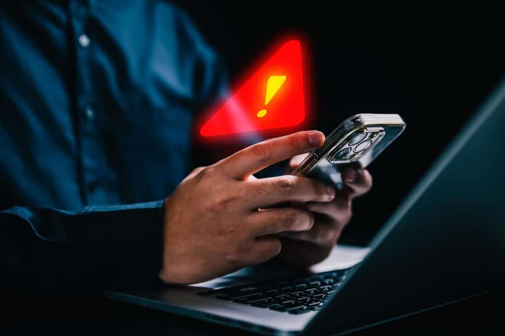 Símbolo de alerta acima de um celular que está sendo usado