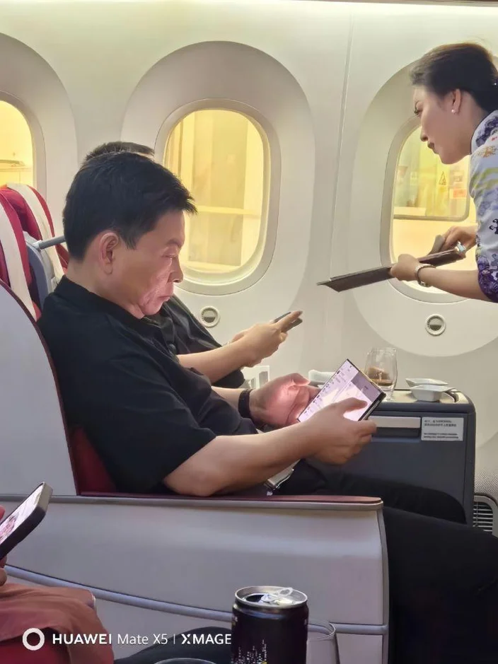 Richard Wu sentado em uma poltrona de avião; de perfil, vemos ele utilizando um smartphone