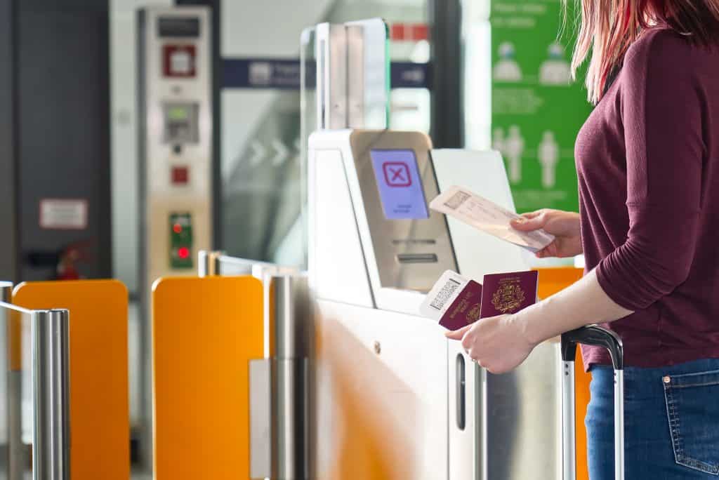 Catraca eletrônica equipada com biometria. Uma mulher está com passaportes na mão esquerda e, na direita, um bilhete de embarque