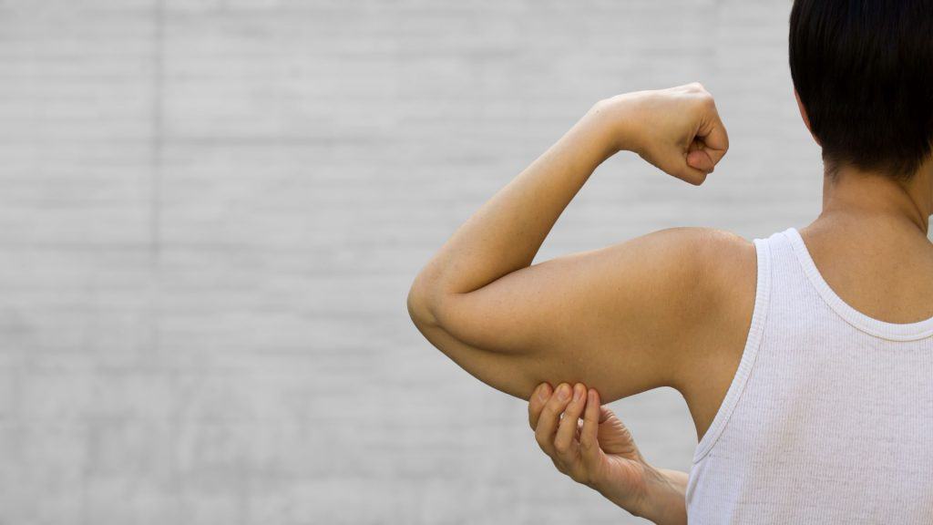 Uma mulher sem rosto mostra os músculos flácidos do braço com o dedo indicador. Síndrome do Braço Flácido (SBF). Efeito do envelhecimento causado pela perda de elasticidade e massa muscular. Banner, espaço para texto.