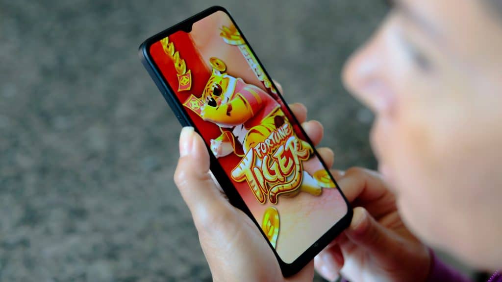 Pessoa olhando para o lado enquanto segura celular com jogo do tigrinho aberto