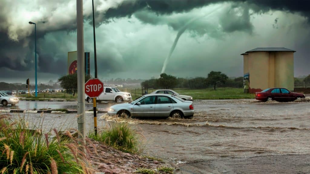 Avenida inundada com carros passando enquanto furacão se forma no horizonte