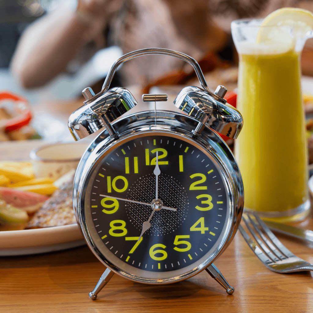 Comer apenas uma vez ao dia faz mal? Conheça os riscos da dieta OMAD O que parece mais uma novidade para emagrecer, a dieta OMAD, se resume em uma outra forma extrema de jejum intermitente. Afinal, esse tipo de estratégia para perder peso consiste em consumir todas as calorias do dia em apenas uma refeição. Mas será que comer uma vez por dia faz bem para a saúde? relógio antigo de mesa e atrás pessoas fazem refeição à mesa.