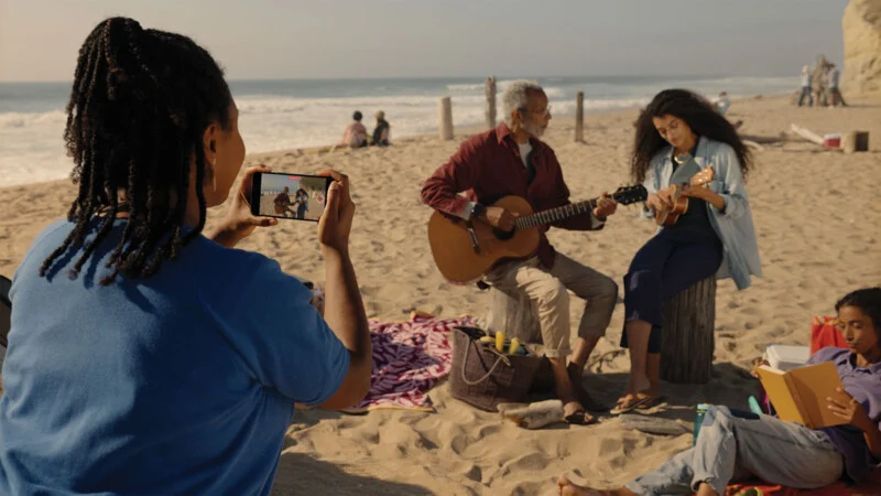 Mulher filmando um homem tocando violão para uma moça em uma praia com um iPhone