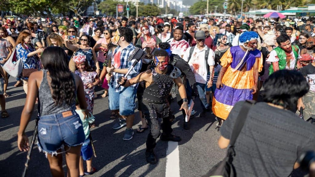 Rio de Janeiro, Brasil - 2 de novembro de 2019: Multidão de zumbis fantasiados avançando na caminhada de Halloween no Dia de Finados, na orla de Copacabana, com palmeiras ao fundo em um dia ensolarado