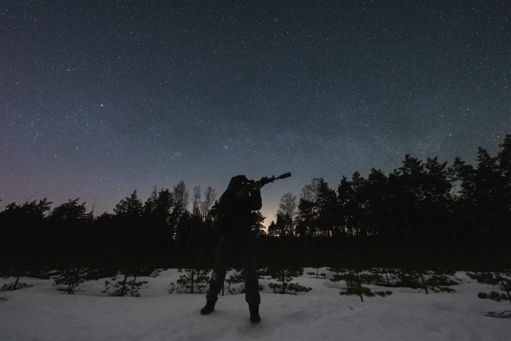 Um soldado com equipamento de visão noturna e um rifle com silenciador e mira laser na floresta