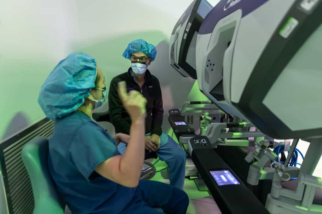 Dois médicos conversando, sentados, em frente de parte do sistema robótico