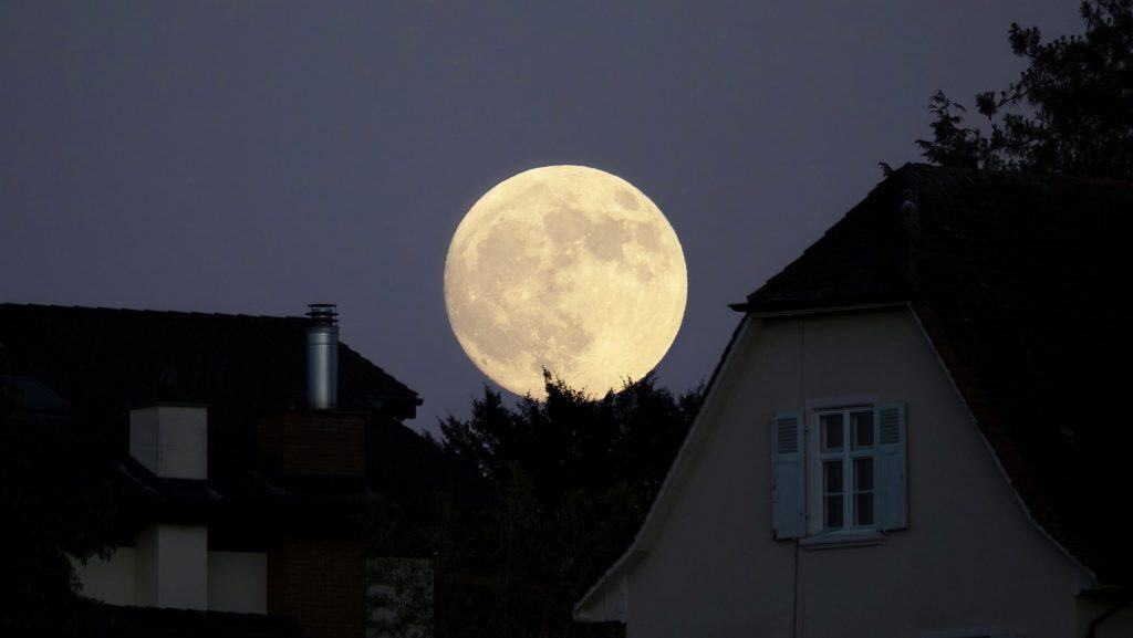 Foto da lua cheia com silhuetas de casas grandes na frente