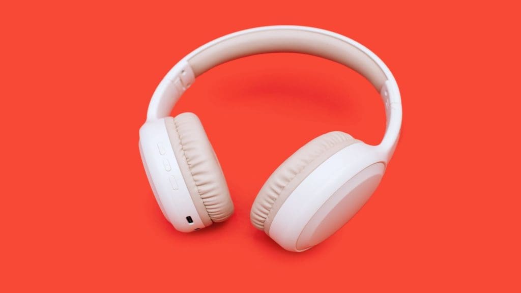 Fones de ouvido sem fio brancos em um fundo laranja brilhante. Fones de ouvido sem fio individuais para jogos e para ouvir faixas de música. Fones de ouvido sem fio over-ear com caminho de recorte. Conceito de música.