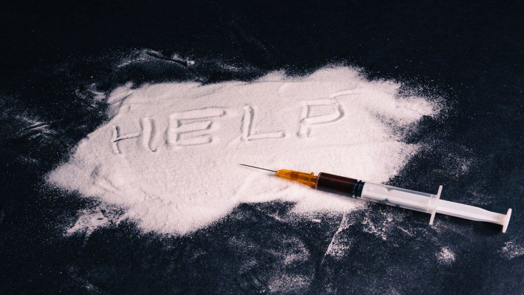 O que a cocaína faz no cérebro e corpo humano? A cocaína é uma droga estimulante poderosa e altamente viciante que afeta diretamente o sistema nervoso central. Seu consumo desencadeia uma cascata de reações químicas no cérebro, gerando uma intensa, porém breve, sensação de euforia e energia. No entanto, os danos que ela causa ao organismo são profundos e duradouros, impactando desde a saúde cardiovascular até o equilíbrio mental. Conceito de dependência química. Heroína é derramada sobre a mesa, a palavra ajuda está escrita nela e há uma seringa com uma dose sobre ela. Fundo preto. Fundo preto. Foto de alta qualidade.