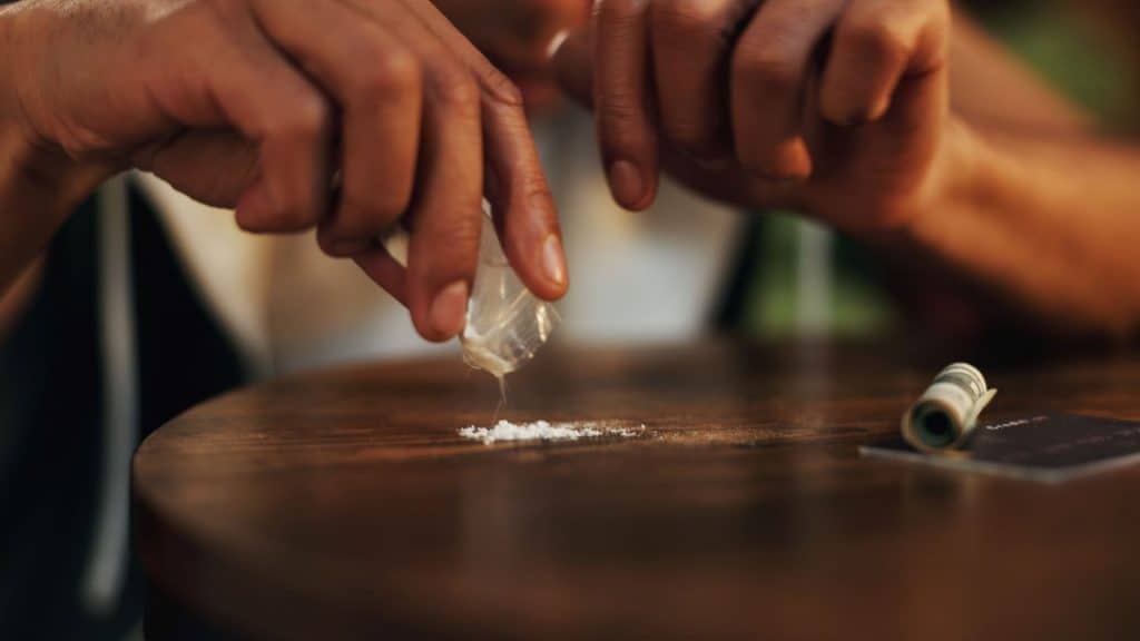 O que é a cocaína rosa? Entenda os riscos que ela representa à saúde Nos últimos anos, emergiu no mercado de drogas uma substância apelidada de cocaína rosa (também chamada de pink cocaine, tusi, tucibi, tuci, entre outros). O nome sugere uma variação da cocaína tradicional, mas na prática raramente contém cocaína pura. Trata-se de uma mistura imprevisível de substâncias psicoativas, muitas delas sintéticas. Pessoa, casa e mão com cocaína, drogas e substância ilegal com vício. Overdose, evento e noite com closeup, hábito ou baixa energia com crime, reabilitação ou cartão de crédito na sala de estar