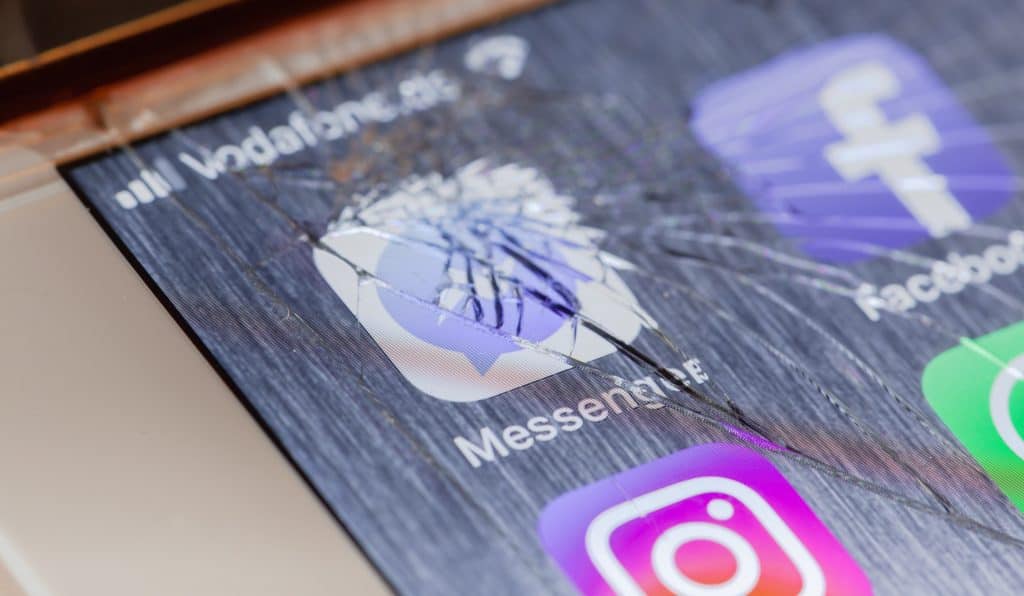 Tela de smartphone quebrada em cima do logo do Messenger