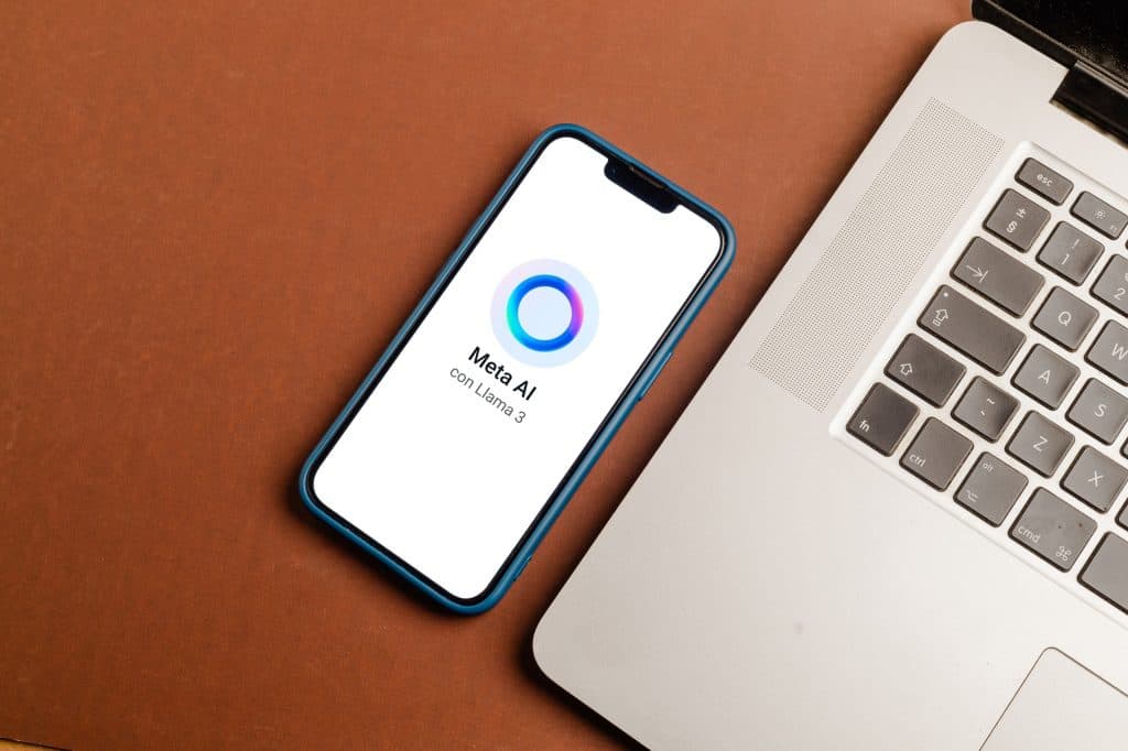 Logo do Meta AI em um smartphone, que repousa ao lado de um notebook