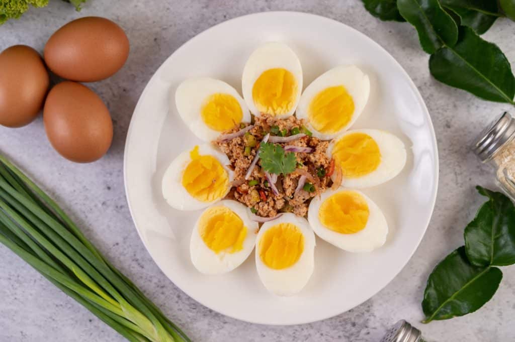 Ovos cozidos cortados ao meio em volta de outro alimento em um prato.