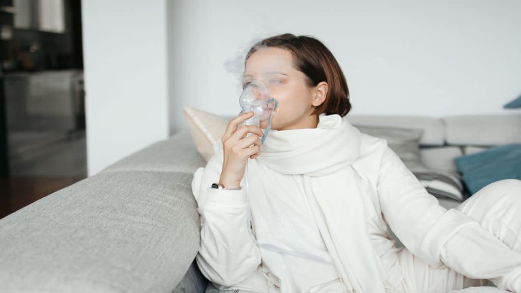 Mulher uando máscara de nebulizador para inalação, sentada no Sofá